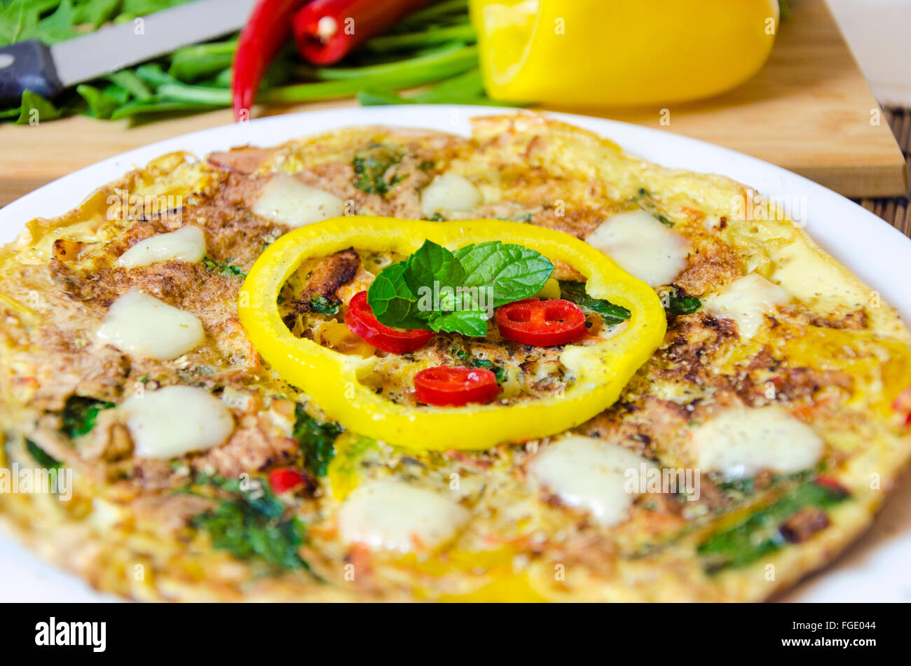 Un spinaci, peperoncino, Menta e Pepe frittata in un piatto sulla tavola di bambù panno e tagliere con coltello e verdure crude. Un Foto Stock