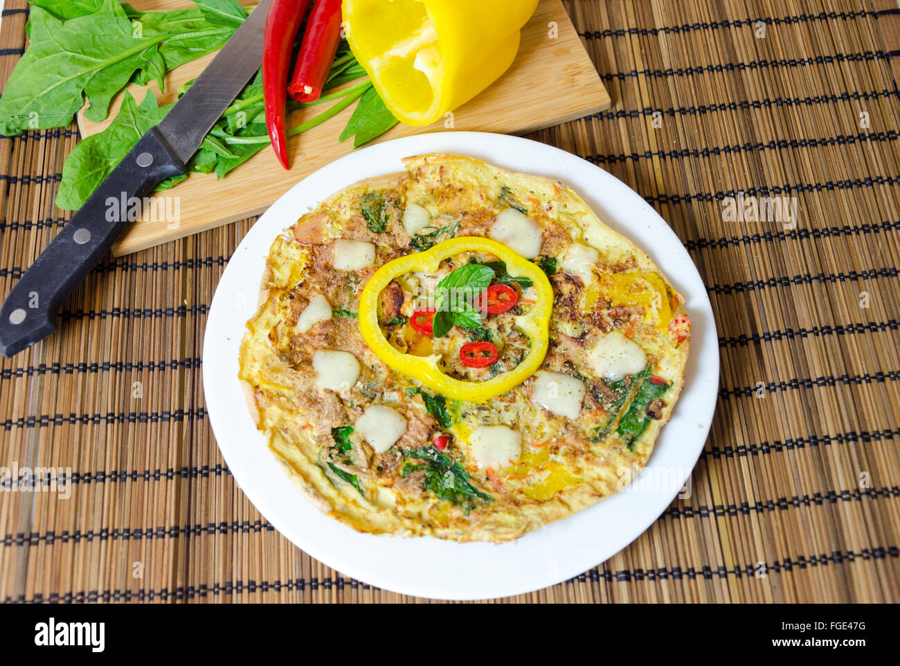 Vista dall'alto di un spinaci, peperoncino, Menta e Pepe frittata in un piatto sulla tavola di bambù panno e tagliere con coltello e materie v Foto Stock