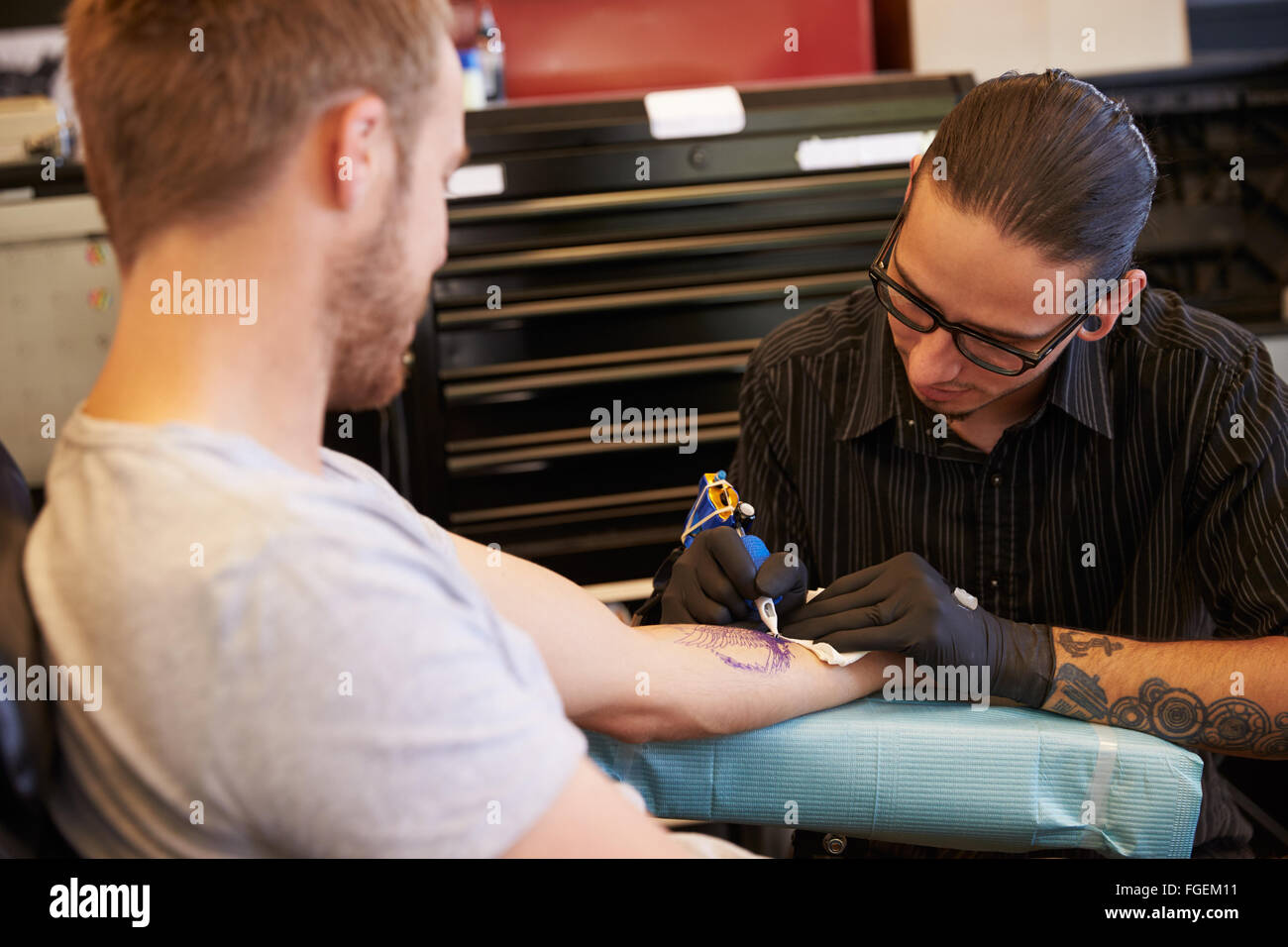 Tatuaggio artista che lavora sul design per Client maschio Foto Stock