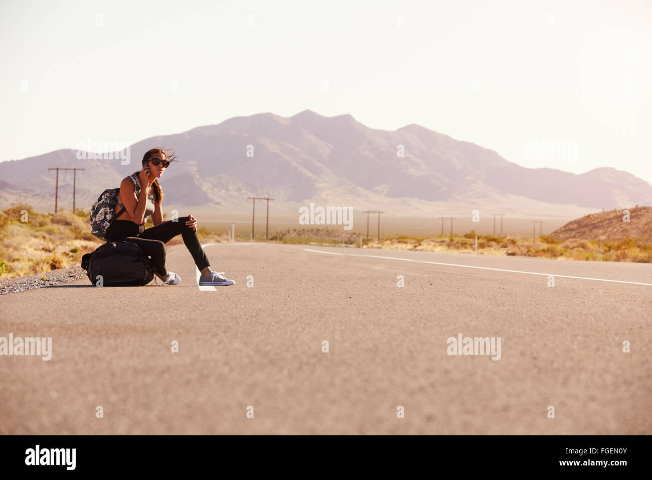 La donna in vacanza autostop lungo la strada utilizzando il telefono cellulare Foto Stock