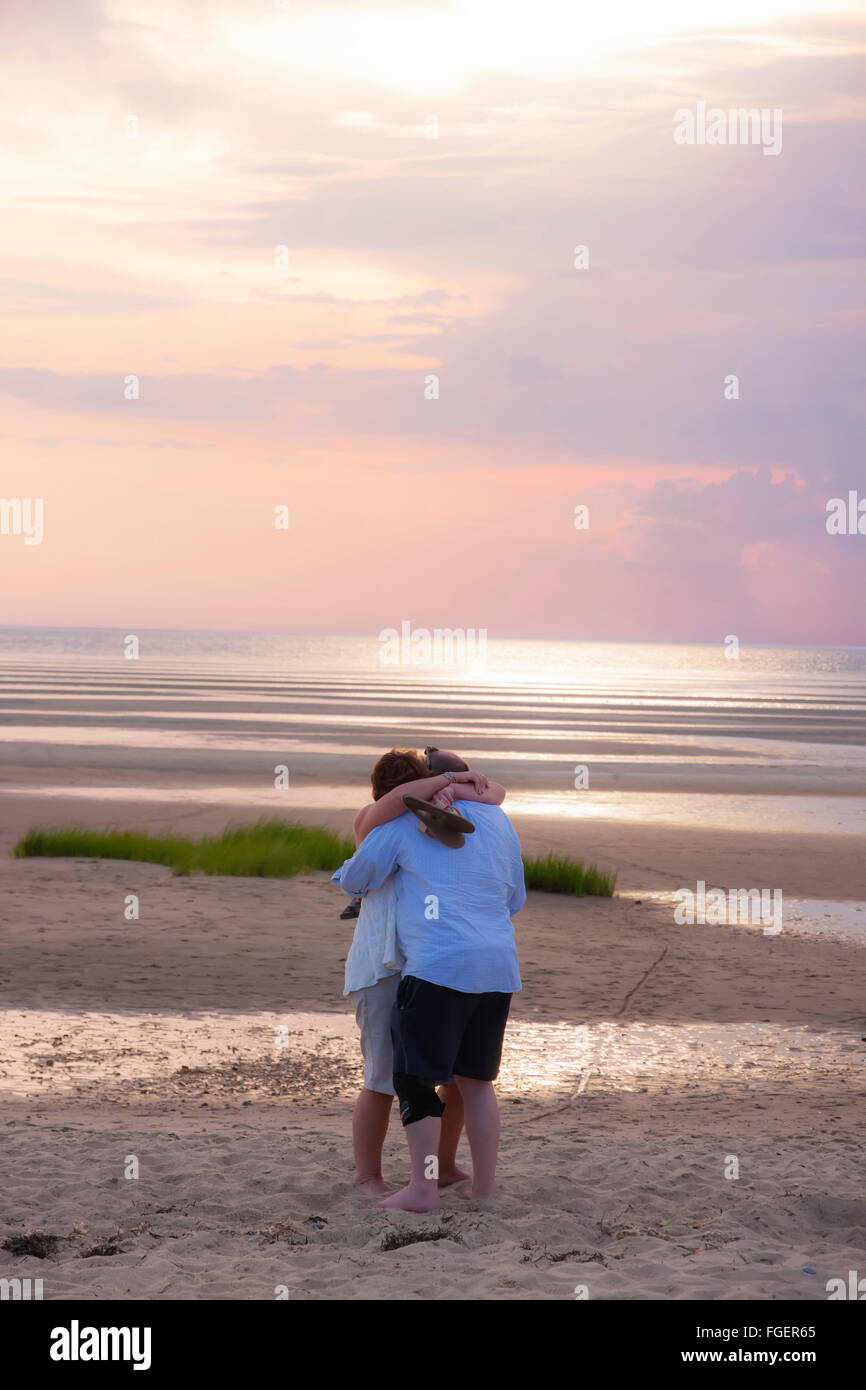 Giovane abbracciando sulla spiaggia al tramonto. Foto Stock