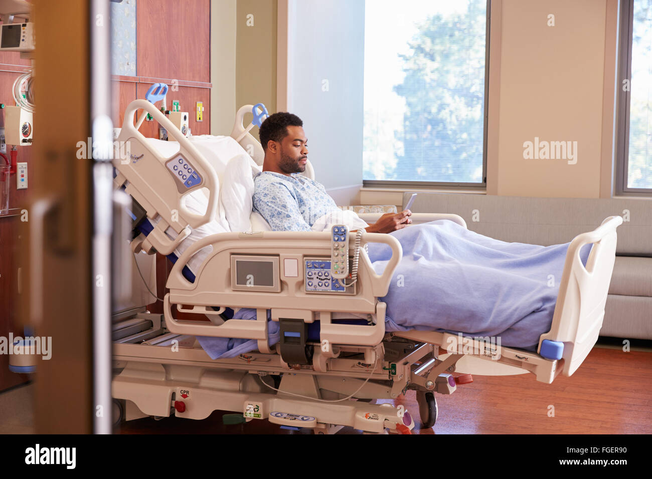 Paziente di sesso maschile nel letto di ospedale tramite cellulare Foto Stock