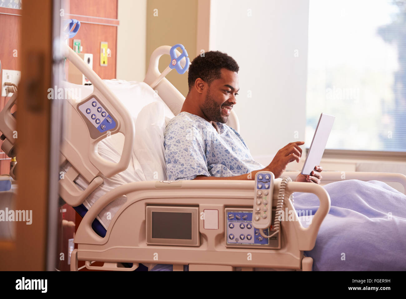 Paziente di sesso maschile nel letto di ospedale con tavoletta digitale Foto Stock
