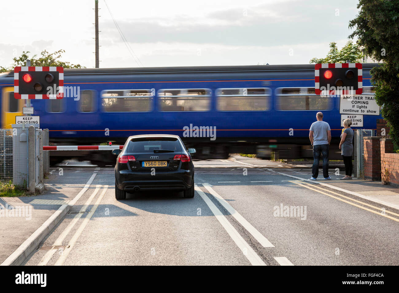 Un auto e persone in attesa presso un passaggio a livello ferroviario come un treno che passa, Attenborough, Nottinghamshire, England, Regno Unito Foto Stock