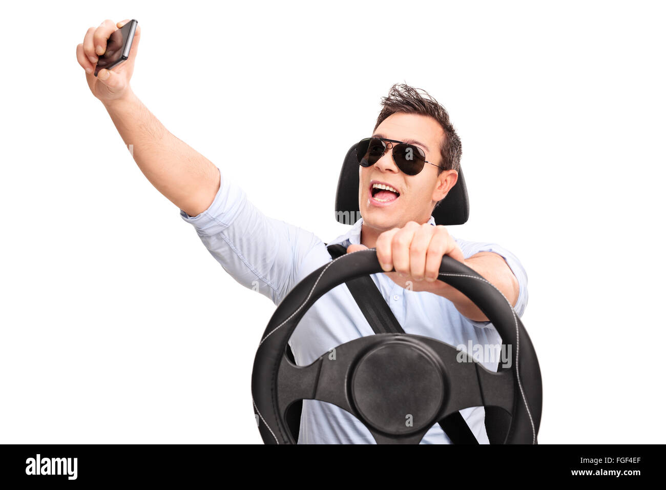 Giovane uomo alla guida e tenendo un selfie con il suo telefono cellulare isolato su sfondo bianco Foto Stock