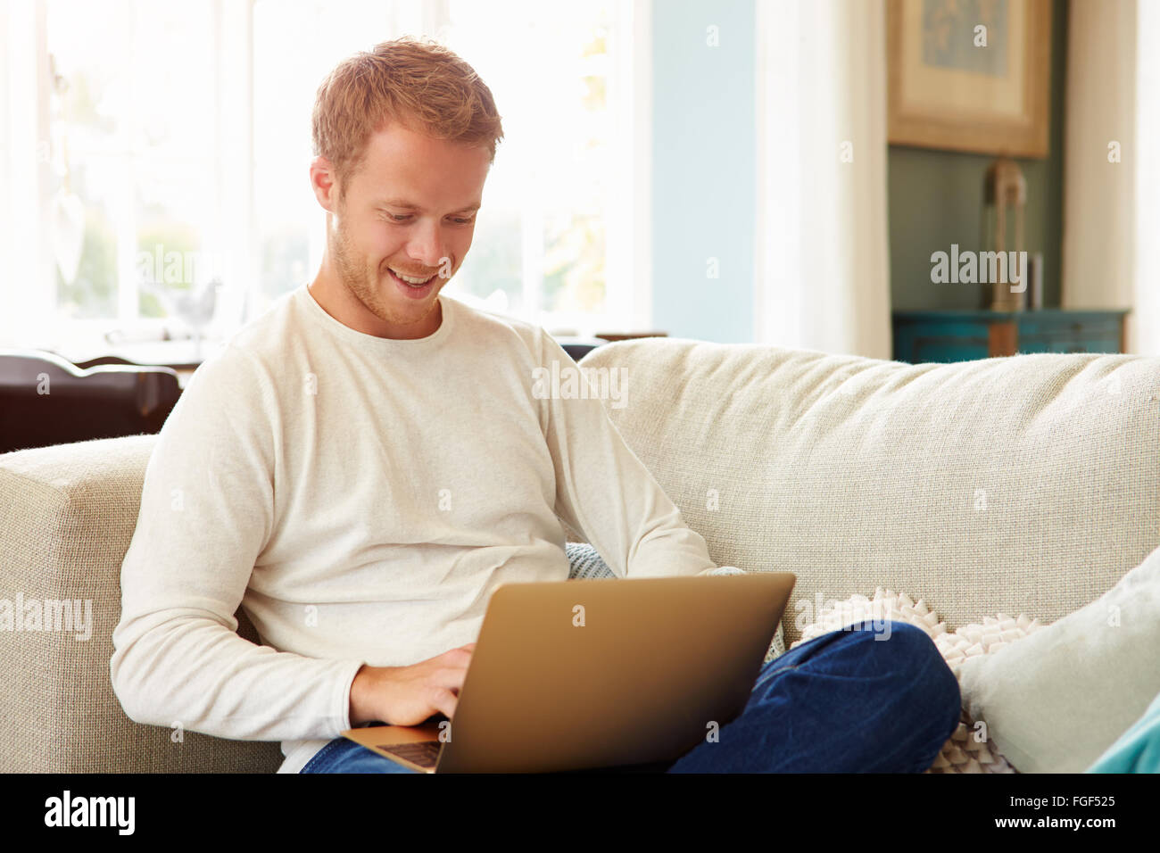 L'uomo rilassante sul divano di casa utilizzando il computer portatile Foto Stock