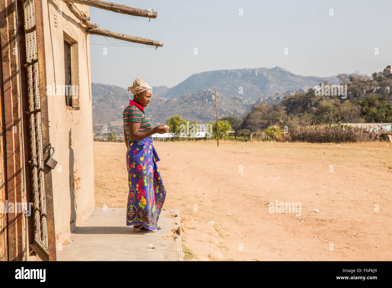 Locale donna dello Zimbabwe sta al di fuori di un edificio nel suo villaggio Foto Stock