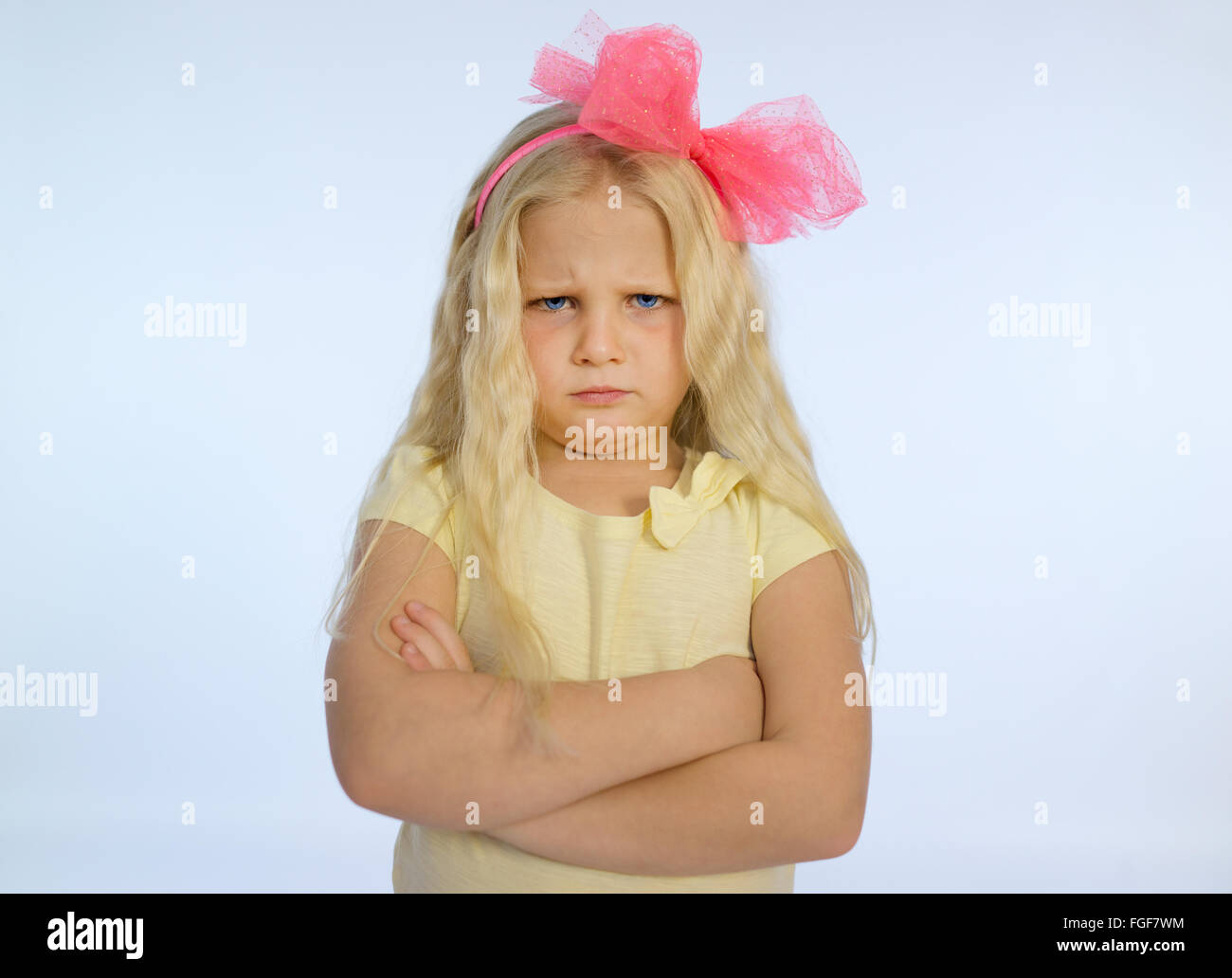 Ragazza giovane con lunghi capelli biondi e bracci ripiegati, accigliata con un triste e scontroso expression Foto Stock