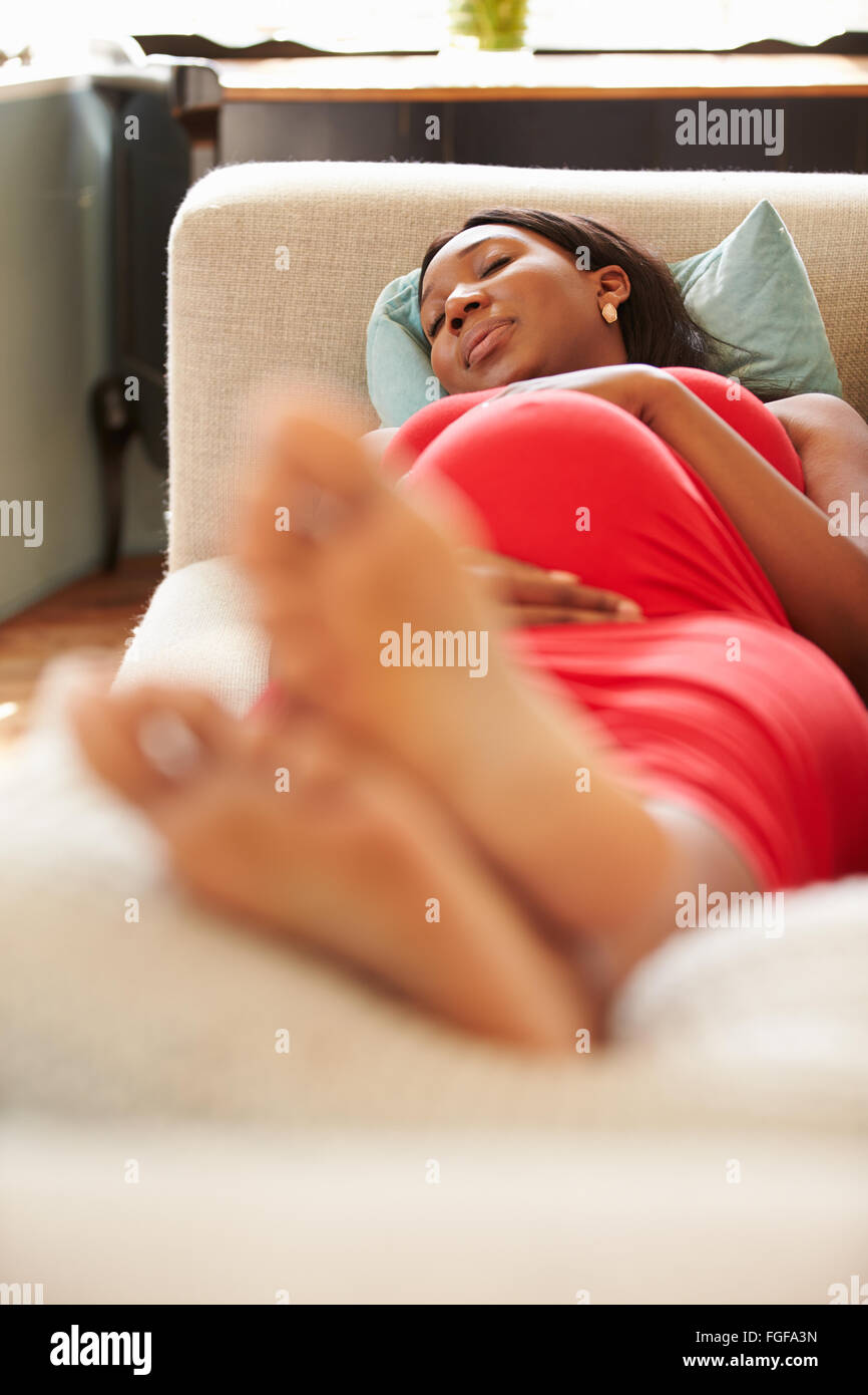 Donna incinta in appoggio sul divano di casa Foto Stock