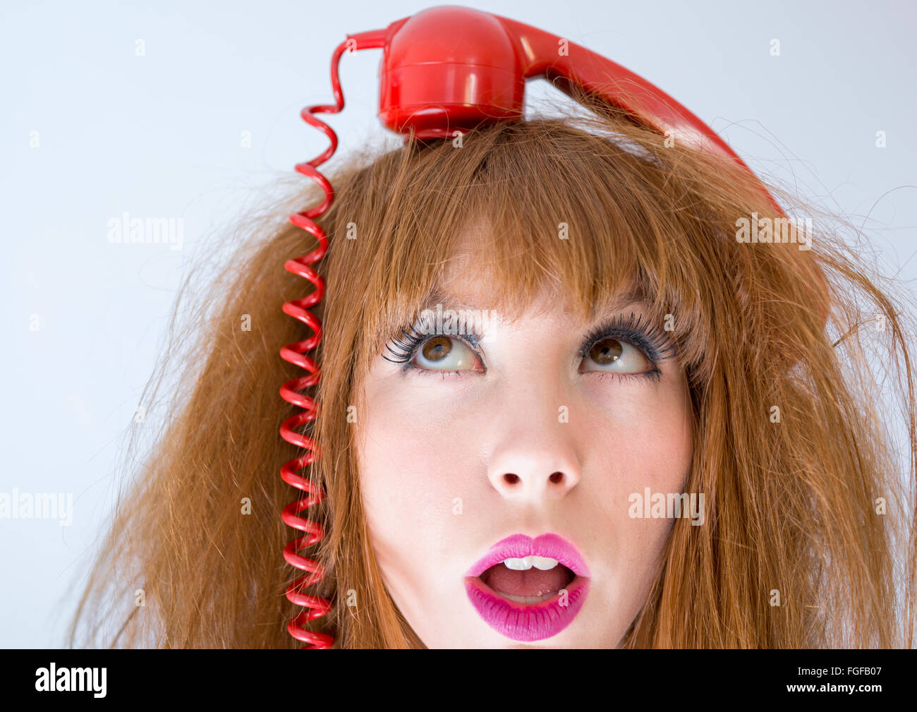 Una donna con il retro rosso telefono bilanciamento del ricevitore sulla parte superiore della sua testa Foto Stock
