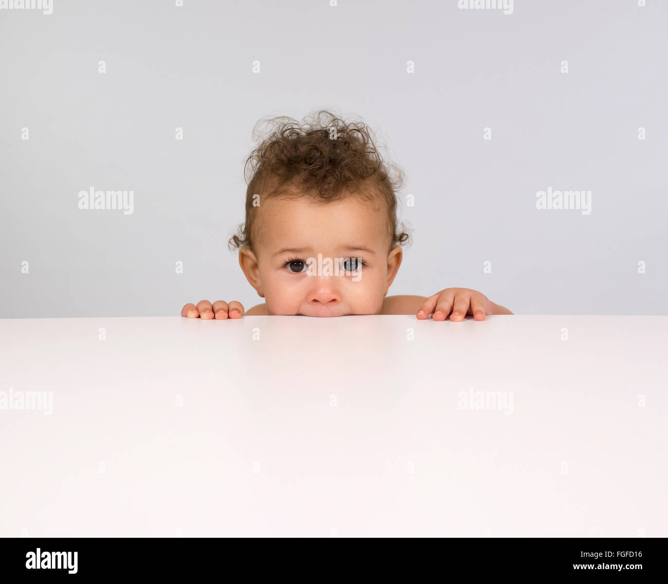 Carino baby boy sbirciando su un tavolo Foto Stock