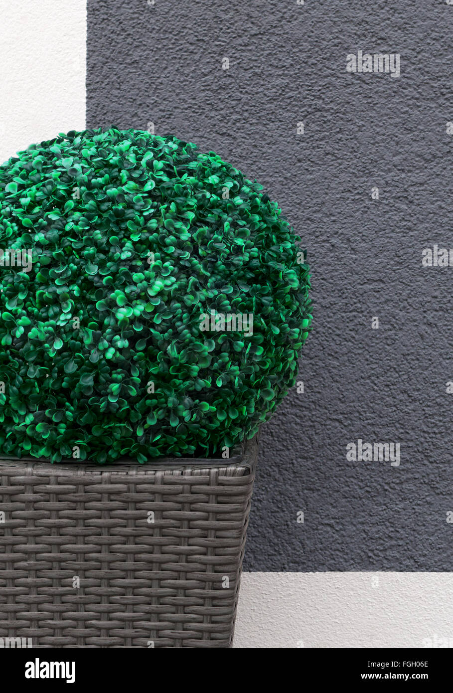 Uno artificiale sfera di legno di bosso in un marrone, intrecciato piantatrice come una decorazione nella parte anteriore di un grigio e bianco muro di casa Foto Stock