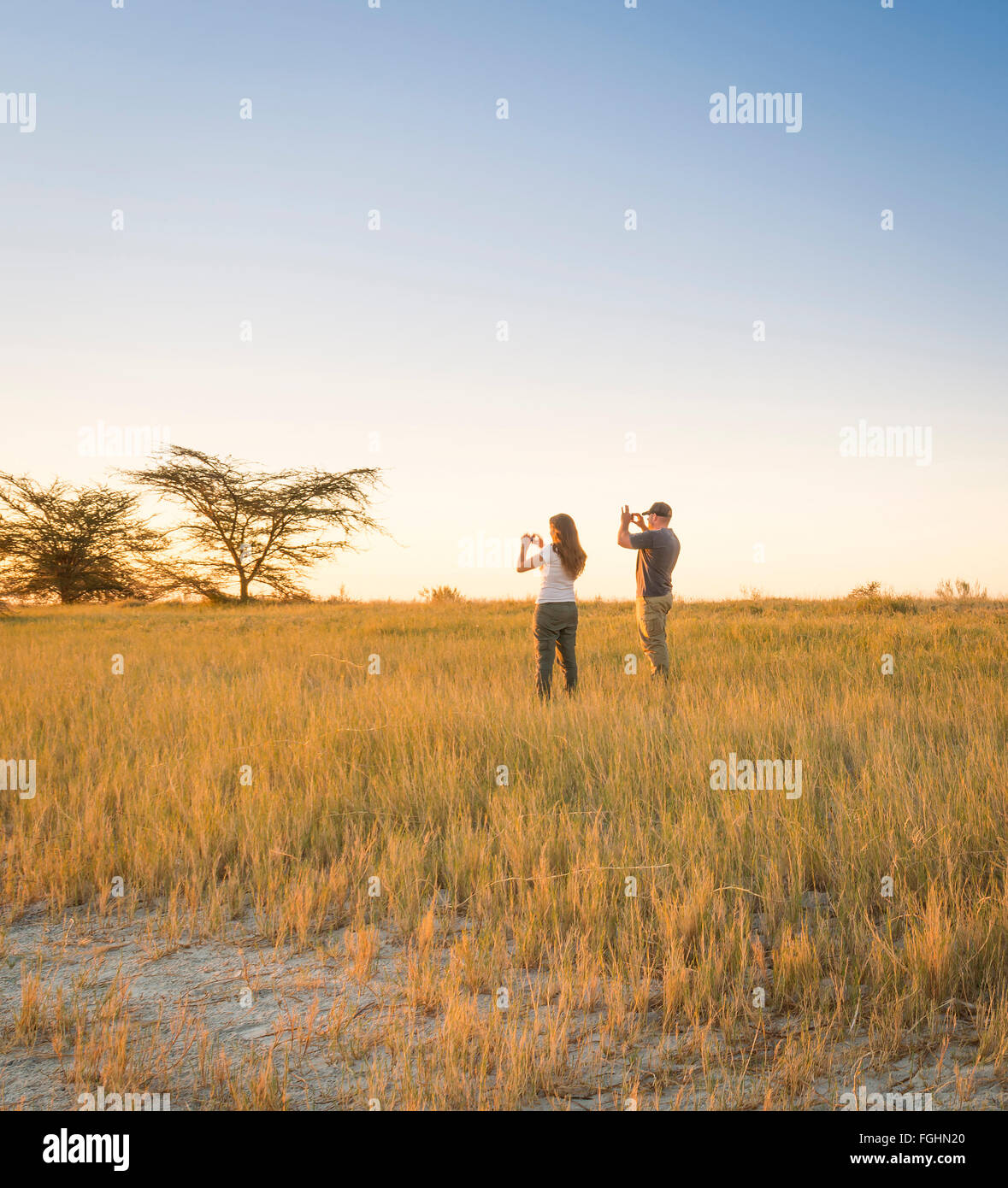 Una giovane coppia di turisti per scattare delle foto di un tramonto Africano mentre su safari in tegami di Makgadikgadi, Botswana Foto Stock