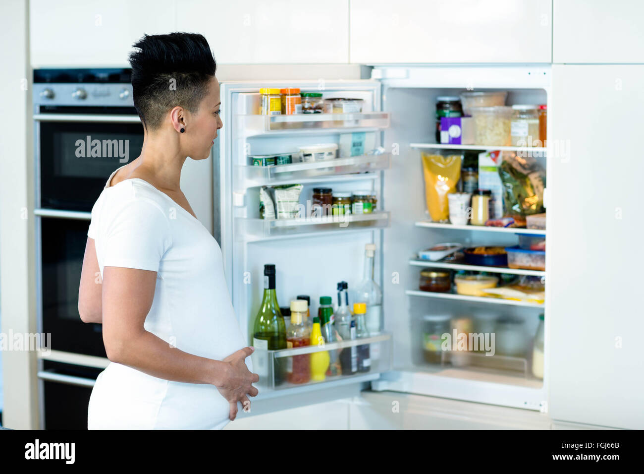 Donna incinta guardando nel frigo Foto Stock
