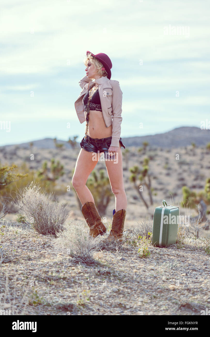 Moda Donna traveler camminando con la valigia e bagagli nel deserto Foto Stock