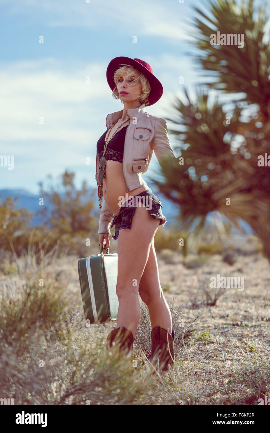 Moda Donna traveler camminando con la valigia e bagagli nel deserto Foto Stock
