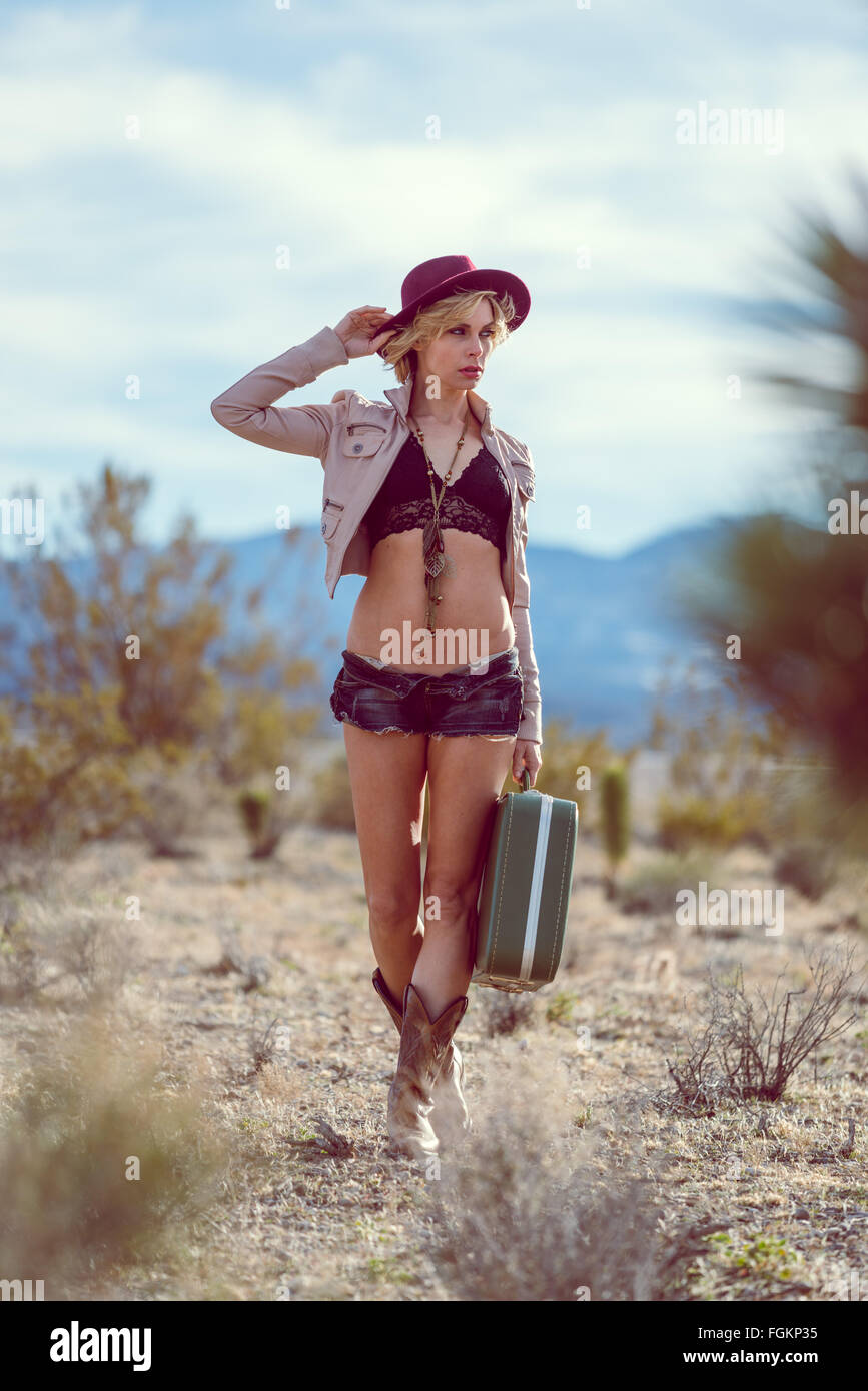 Moda Donna traveler camminando con la valigia e bagagli nel deserto Foto Stock