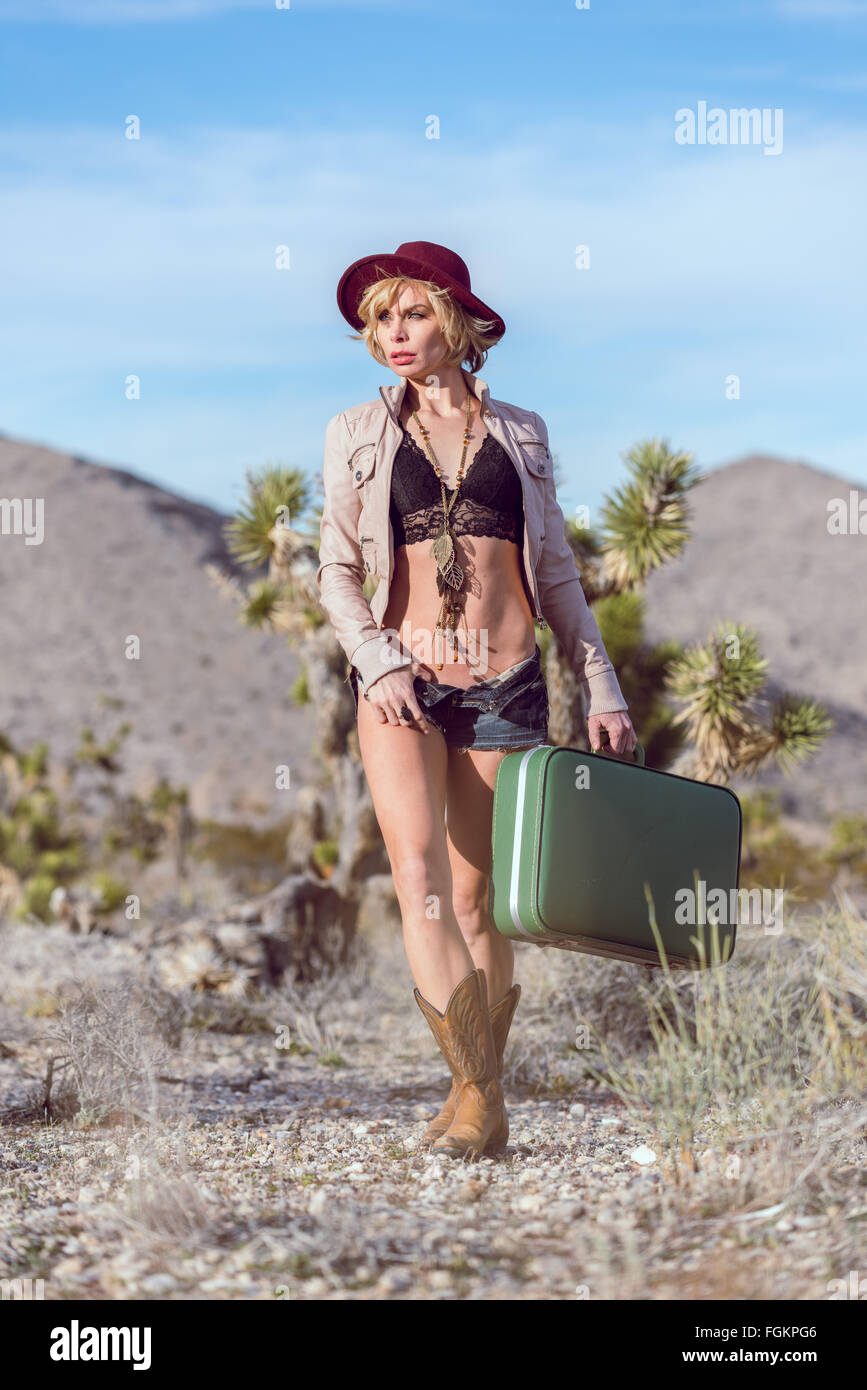 Moda Donna traveler camminando con la valigia e bagagli nel deserto Foto Stock