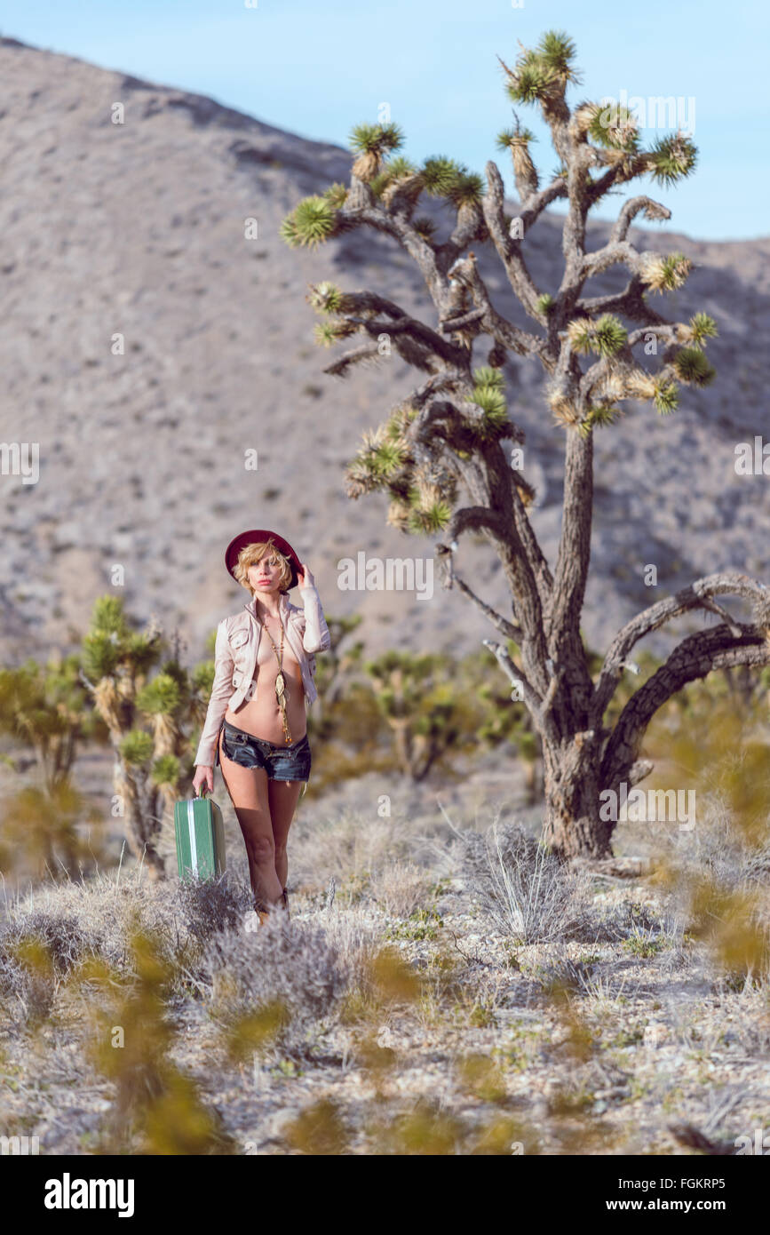 Moda Donna traveler camminando con la valigia e bagagli nel deserto Foto Stock