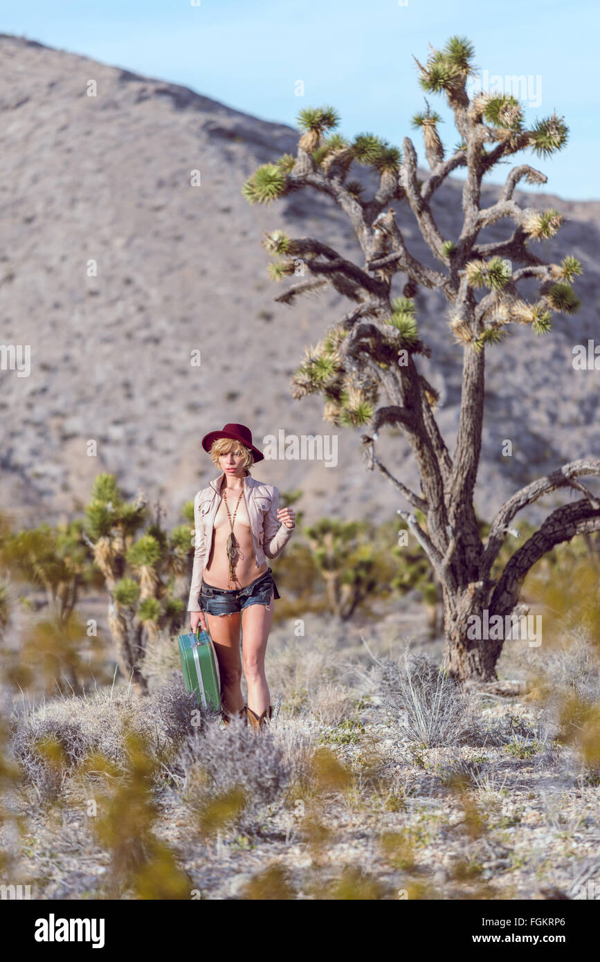 Moda Donna traveler camminando con la valigia e bagagli nel deserto Foto Stock