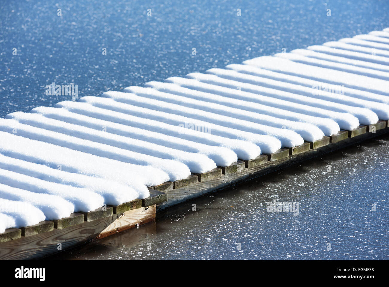 Linee parallele di neve su un molo in legno in acqua congelata in inverno. Foto Stock