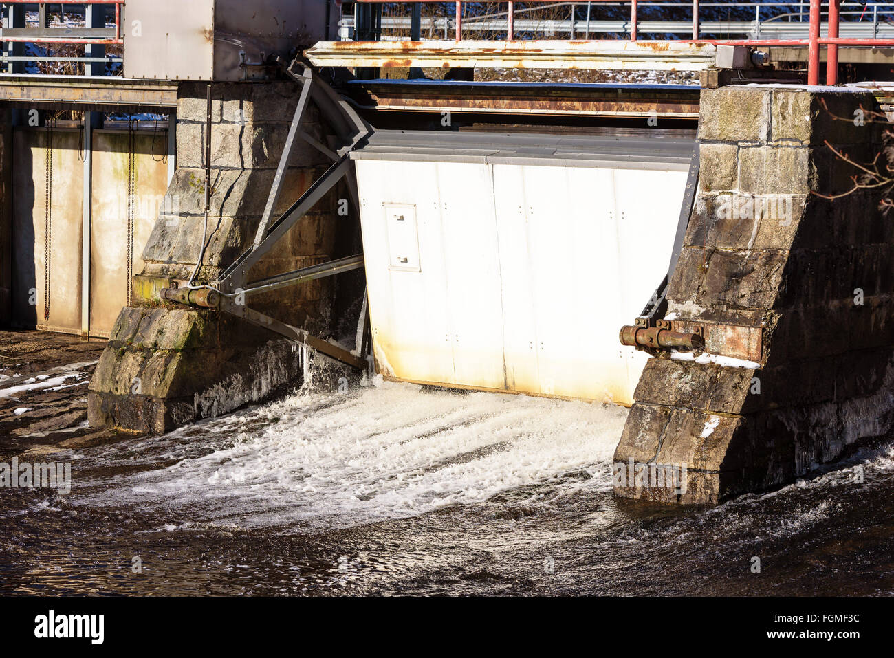 Un trafilamento di acqua fuoriesce sotto una chiusa saracinesca in corrispondenza di una piccola diga idroelettrica. Foto Stock