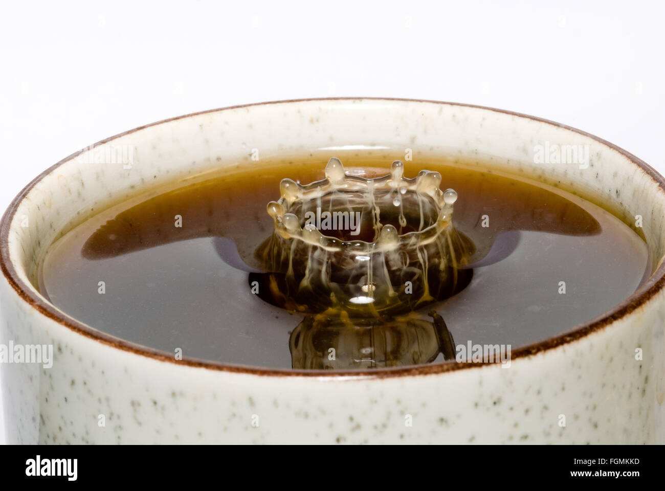 Goccia di latte di cadere nella tazza di caffè nero di miscelazione e di schizzi di goccioline di discesa creazione di motivi forme Increspature nella superficie tazza da tè Foto Stock