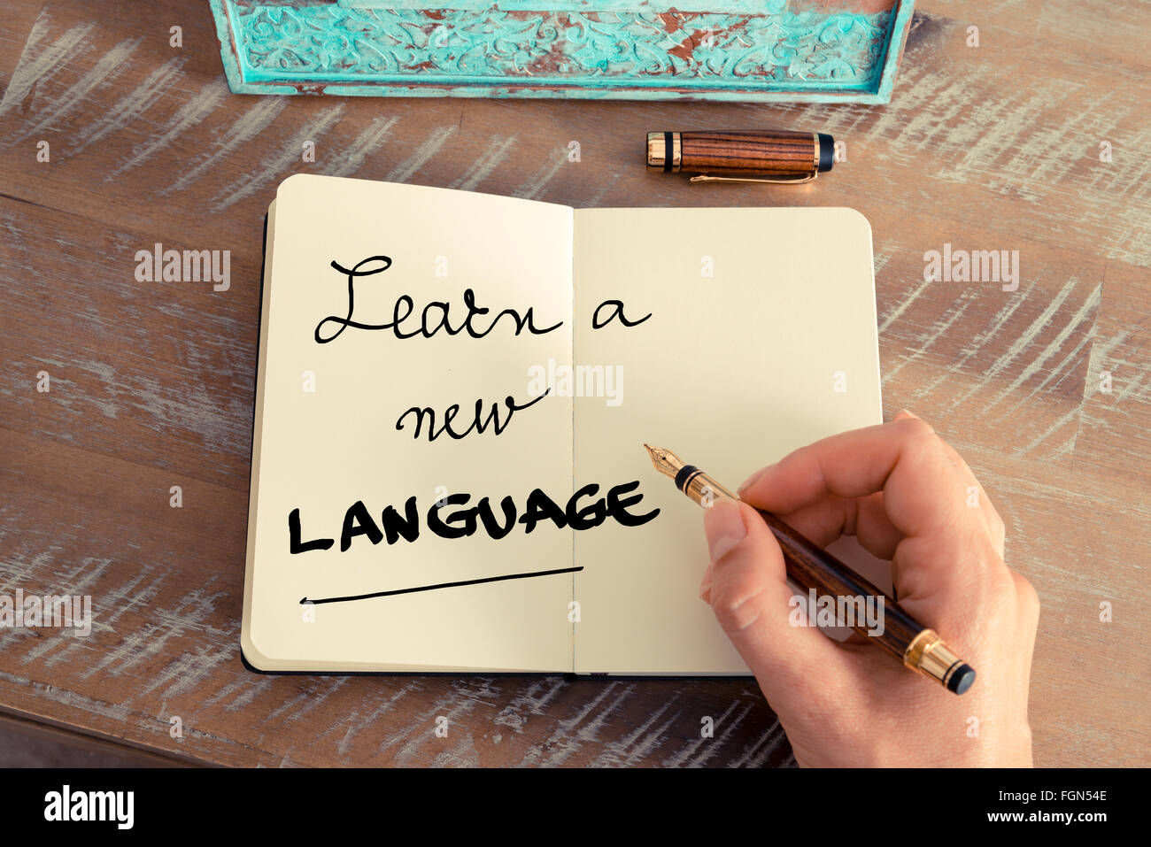 Effetto retrò e tonico immagine di una donna la scrittura a mano una nota con una penna stilografica su un notebook. Concetto motivazionale con il testo scritto a mano imparare una nuova lingua Foto Stock