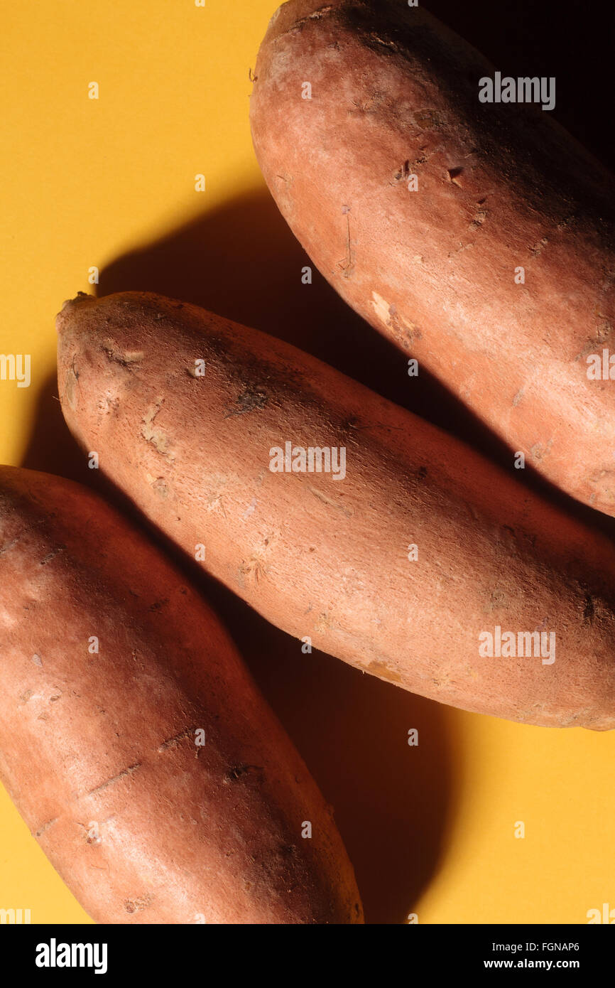 Tre patate dolci (patate) su uno sfondo giallo. Foto Stock