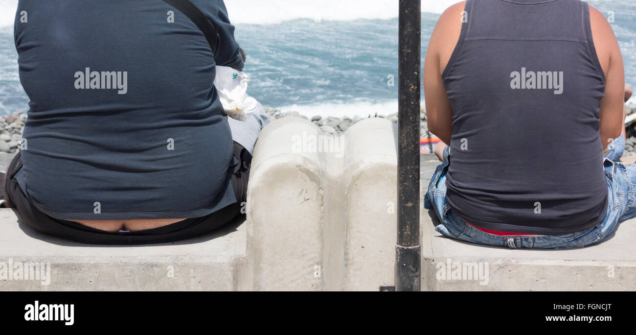 Due uomini, uno in sovrappeso con builder bum guardando al mare Foto Stock