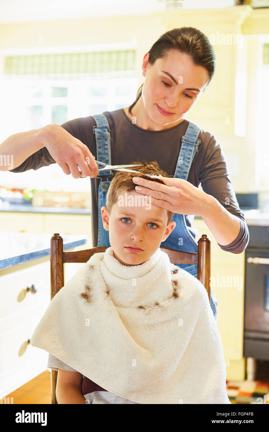 Ritratto infelice ragazzo getting taglio di capelli da madre in cucina Foto Stock