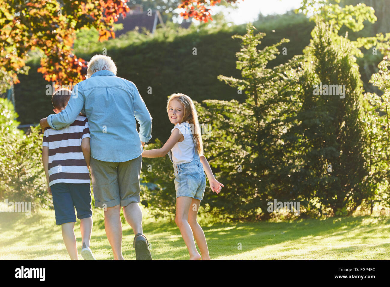 Ritratto sorridente ragazza camminare con la nonna e il fratello in giardino Foto Stock