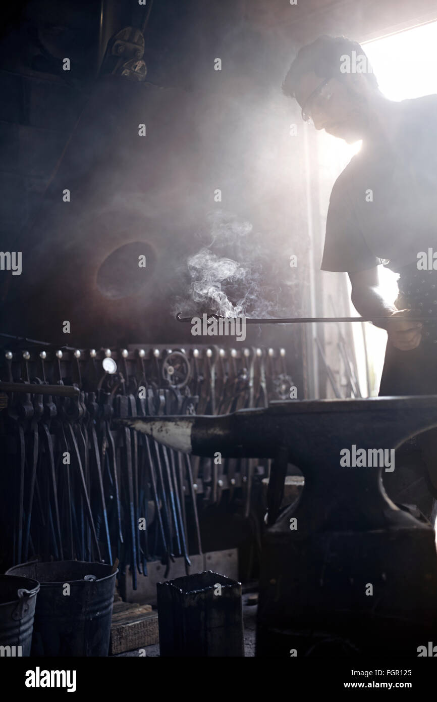 Fabbro tenendo la cottura a vapore del ferro battuto su incudine nella fucina Foto Stock