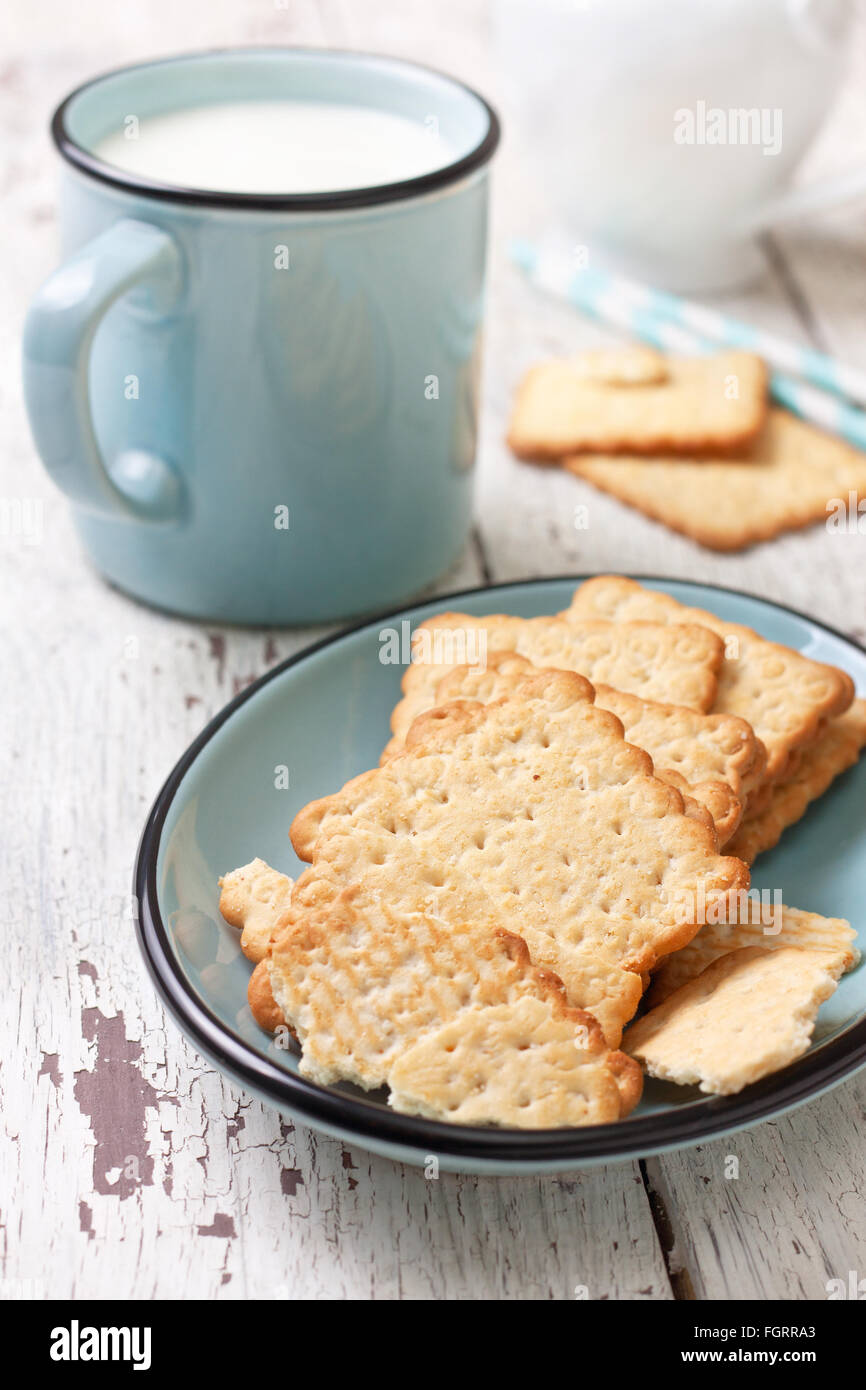 Crackers su una lastra blu e una tazza di latte su un bianco sullo sfondo di legno Foto Stock