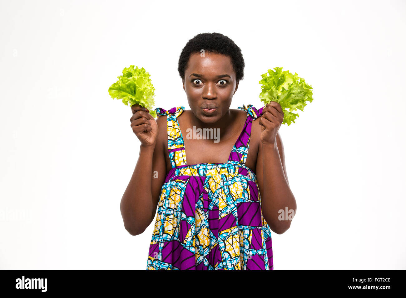 Funny eccitato americano africano giovane donna in colorate sundress trattenere foglie di lattuga su sfondo bianco Foto Stock