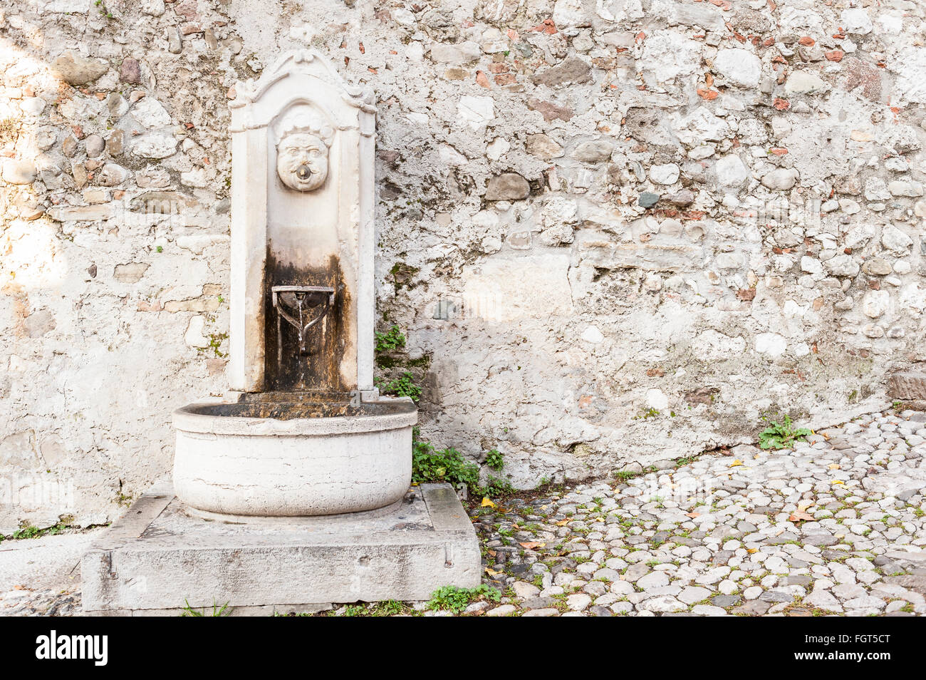 Il vecchio e la piccola fontana di pietra con il bambino faccia. Foto Stock