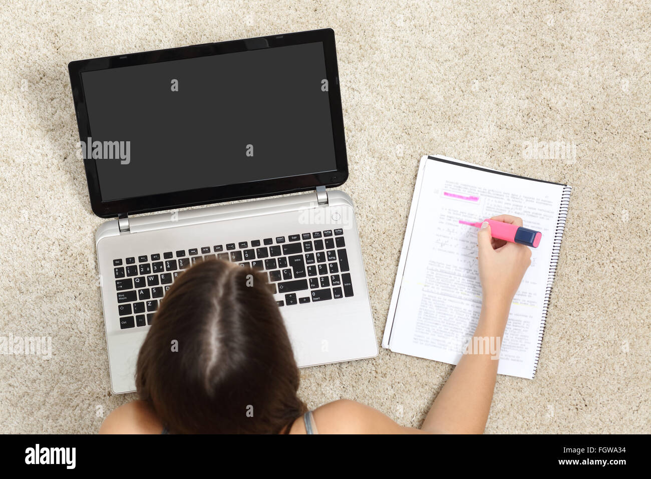 Ragazza a studiare con un computer portatile e evidenziando in un notebook sdraiato sul pavimento a casa Foto Stock