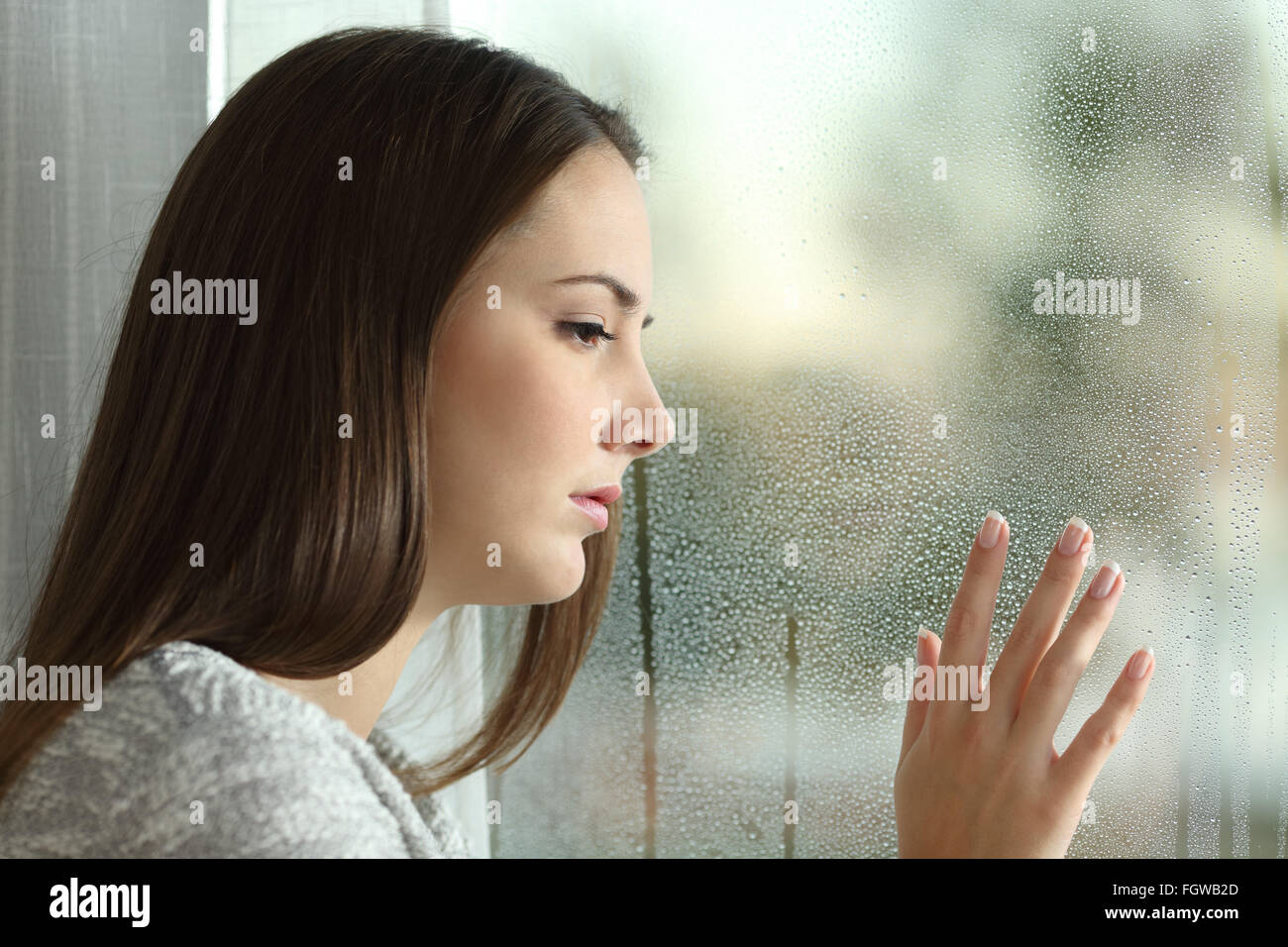 Triste donna che guarda la pioggia caduta attraverso una finestra a casa o in albergo Foto Stock