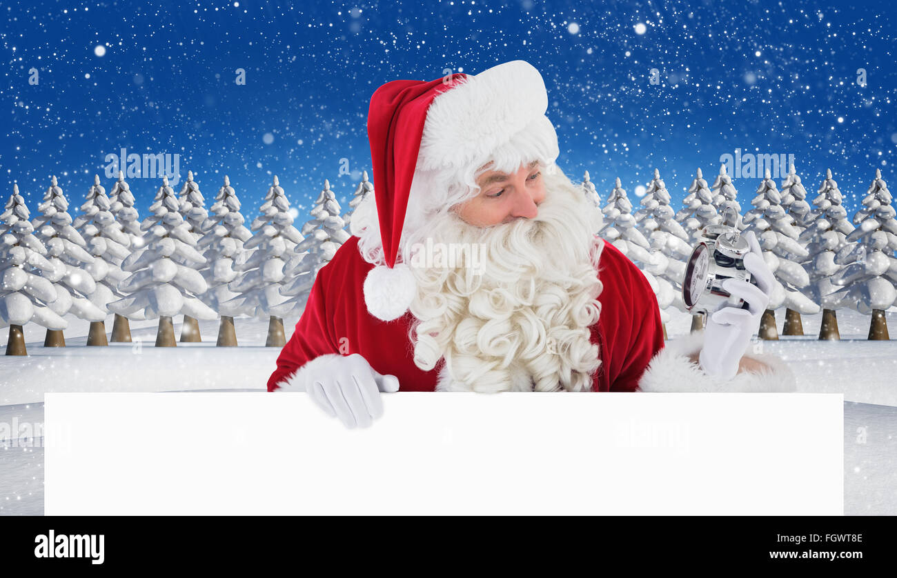 Immagine composita di felice santa tenendo sveglia e firmare Foto Stock