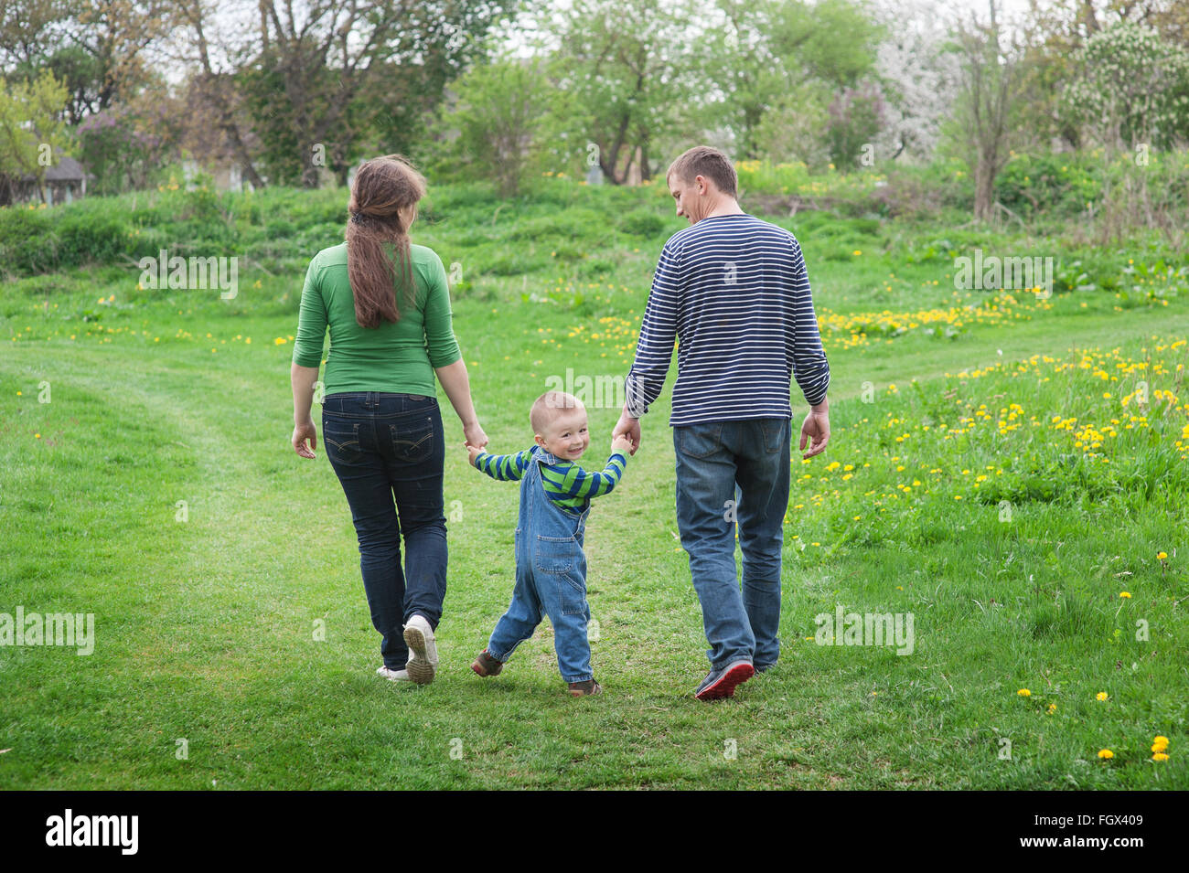 I genitori sono a piedi con un ragazzino su un verde prato primavera su un sentiero Foto Stock
