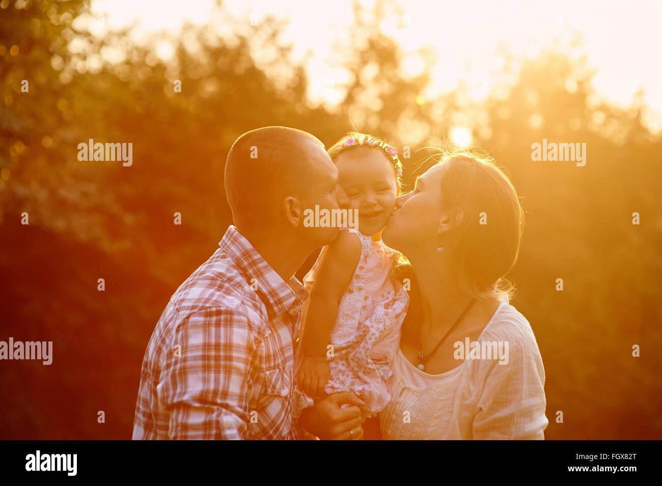 La famiglia felice mamma e papà tenendo la figlia nelle sue braccia e baciarla nel parco Foto Stock
