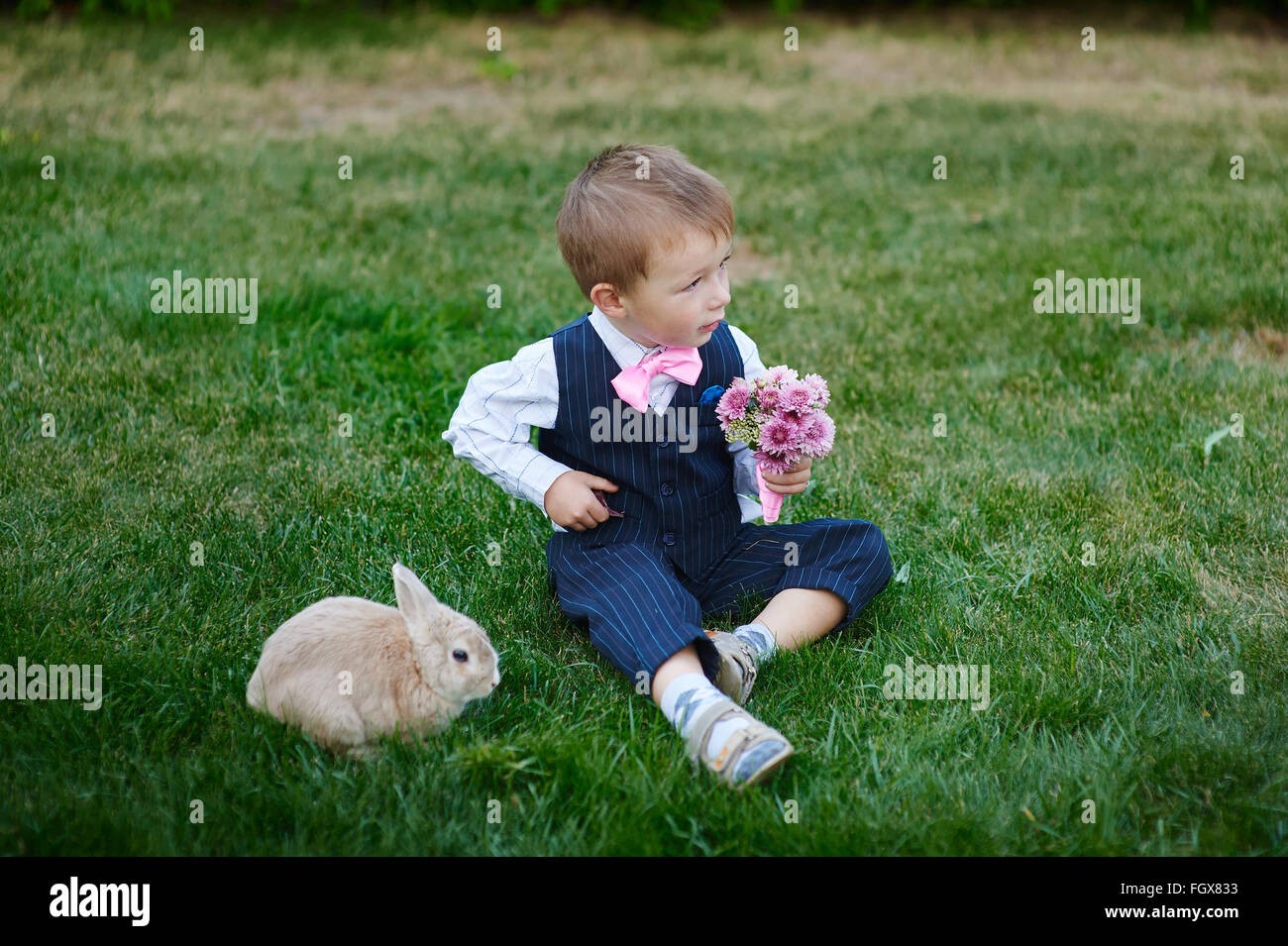 Little Boy in tuta con un mazzo di fiori e un coniglio Foto Stock