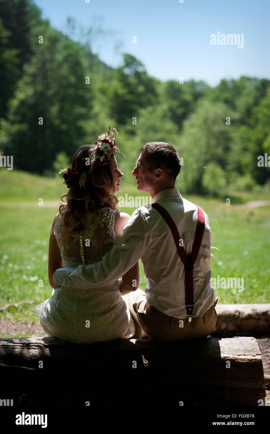 Elegante sposi sposa in abito bianco e sposo elegante seduta su una panchina nel parco Foto Stock