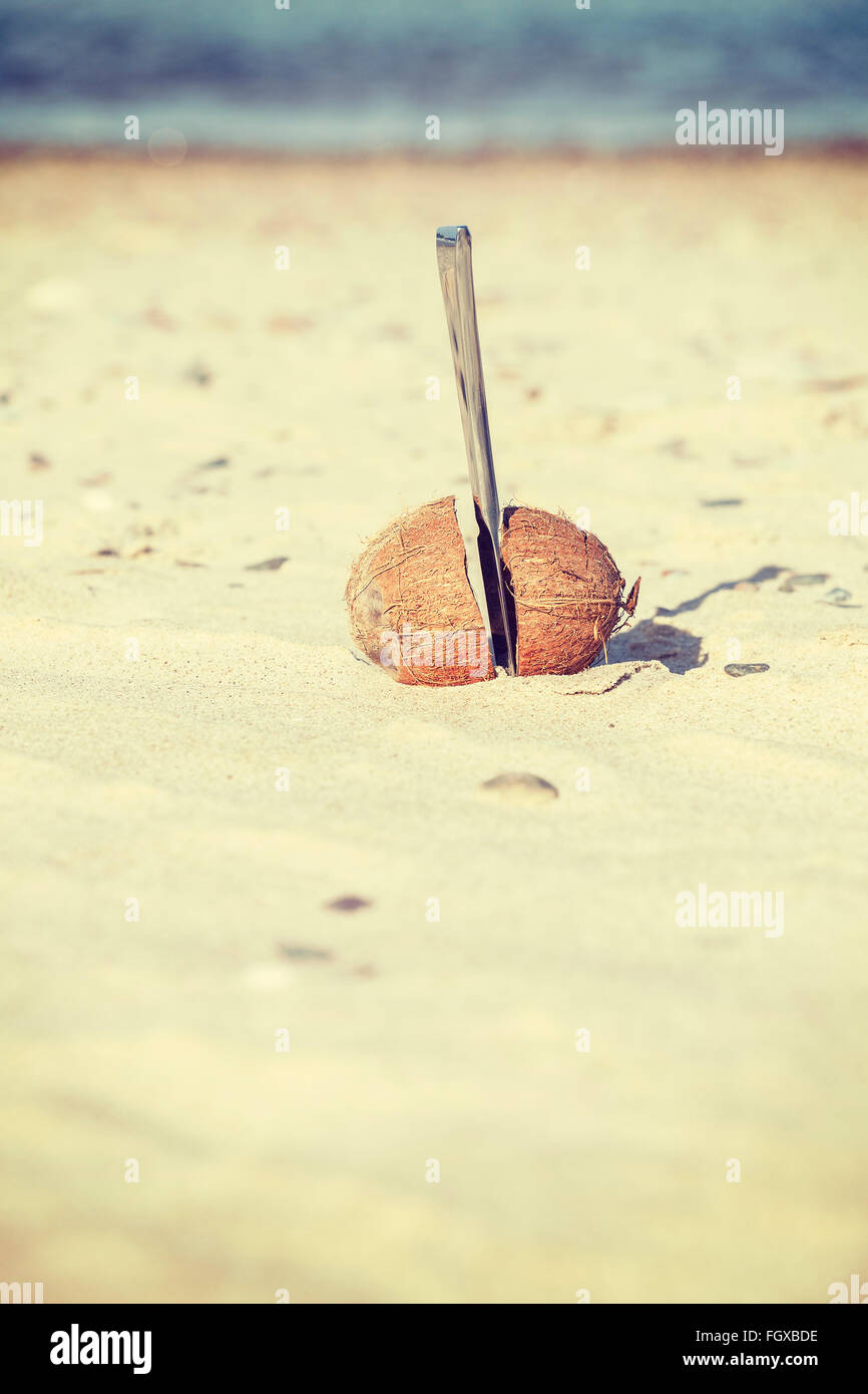 Vintage tonica il cocco tagliato a metà con un coltello su una spiaggia. Foto Stock