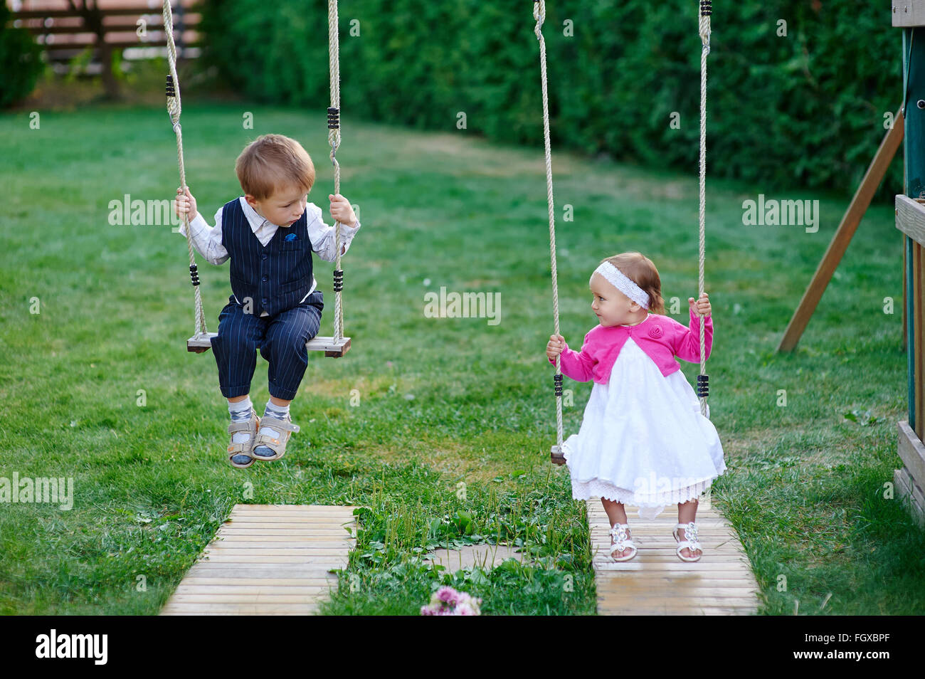 Piccolo Ragazzo e ragazza ride su uno swing presso il parco giochi nel parco Foto Stock