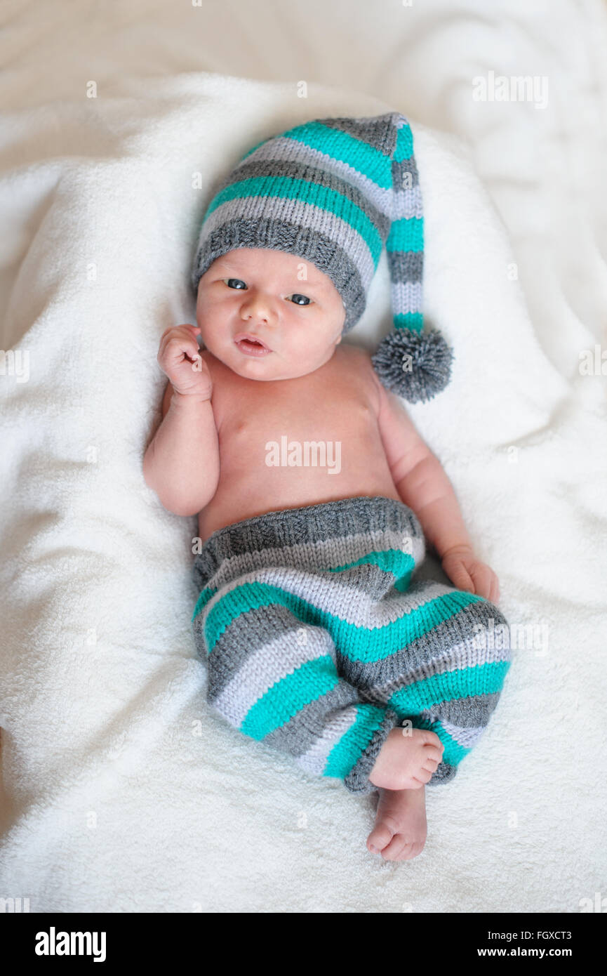 Little baby boy in un berretto lavorato a maglia giacente sul letto bianco Foto Stock