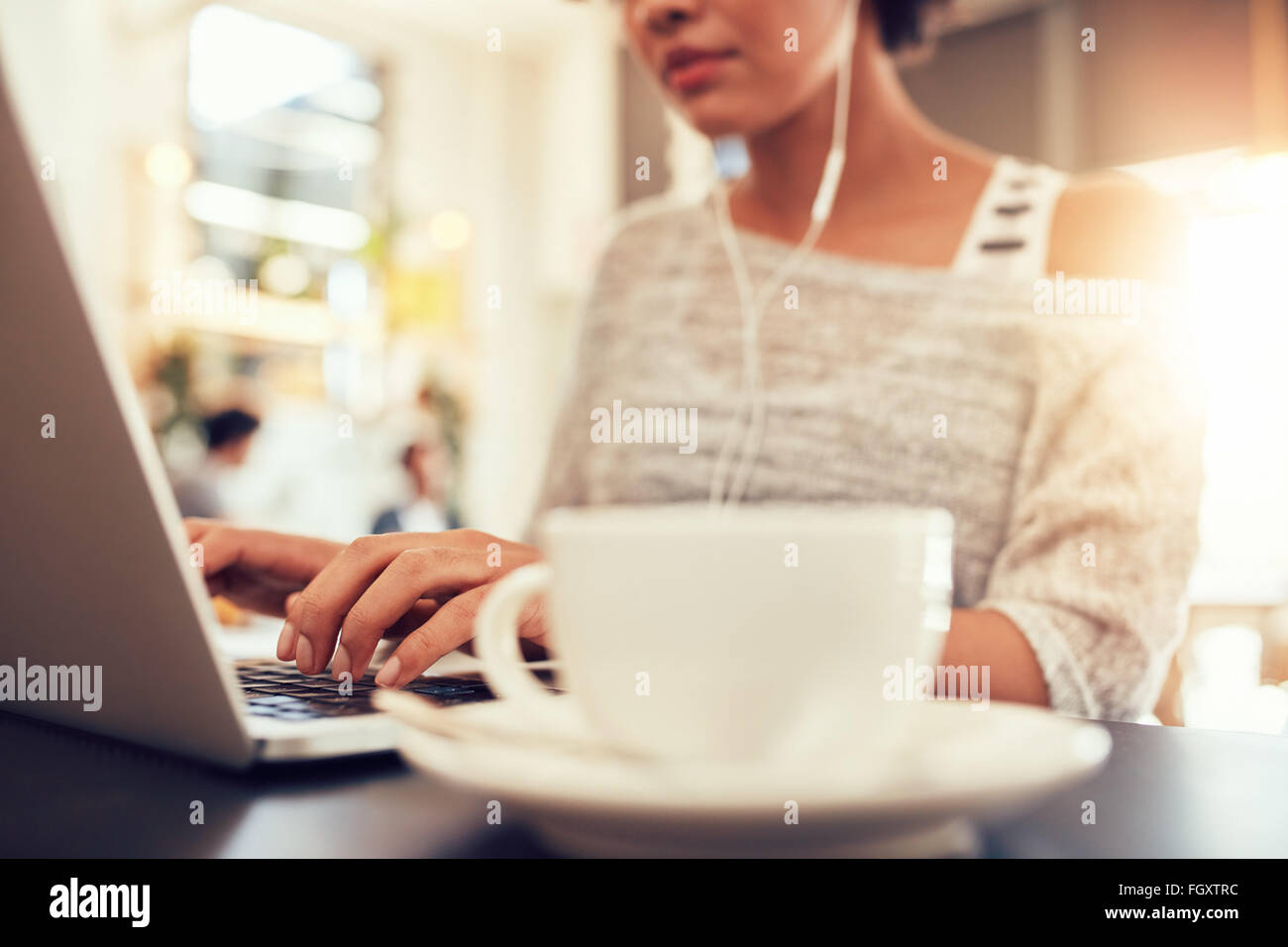 Donna seduta a un coffee shop lavorando sul computer portatile, con focus su mani digitando sulla tastiera. Foto Stock