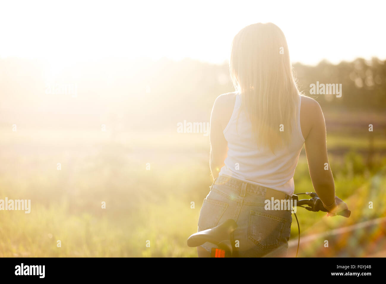 Vista posteriore di sportivo bella giovane donna sulla bici indossando casual serbatoio bianco superiore e gli shorts in denim in una giornata di sole in estate Foto Stock