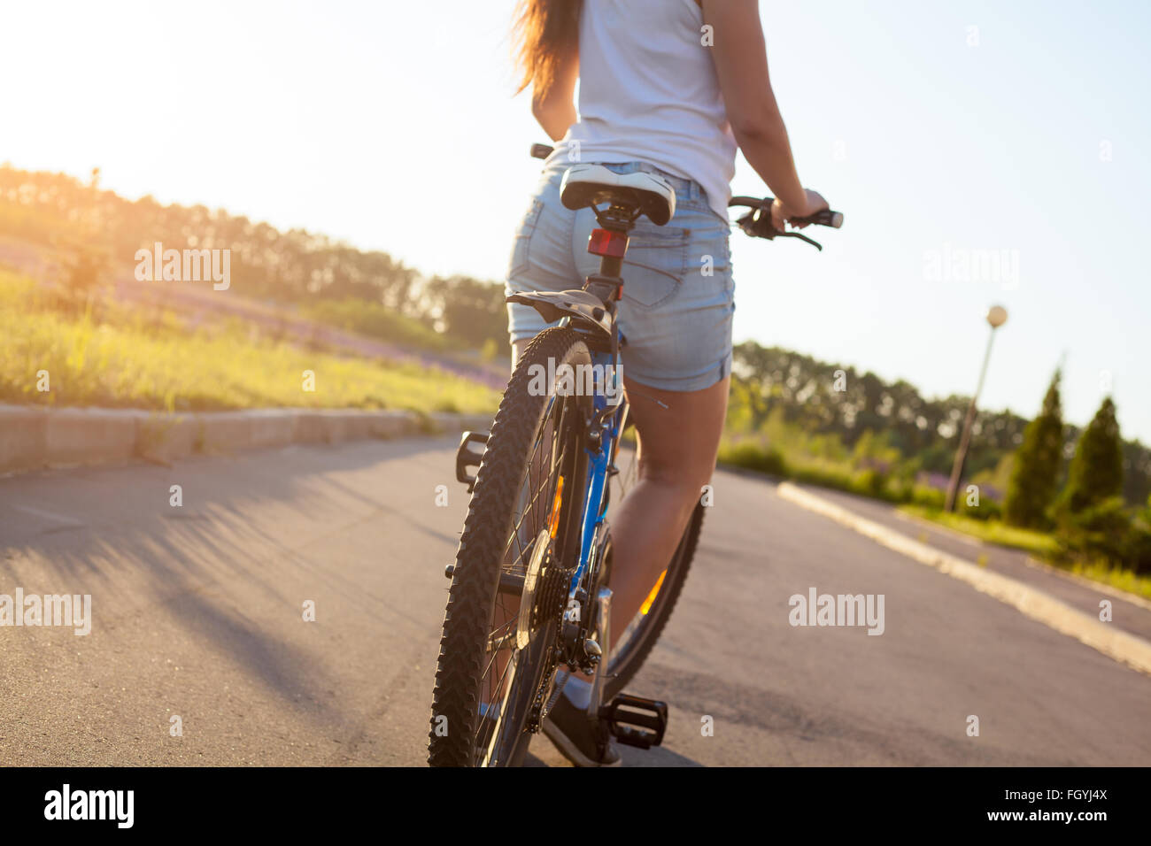 Sporty bella giovane donna a partire in mountain bike casual da indossare vestiti di bianco su strada in condizioni di luce solare intensa Foto Stock