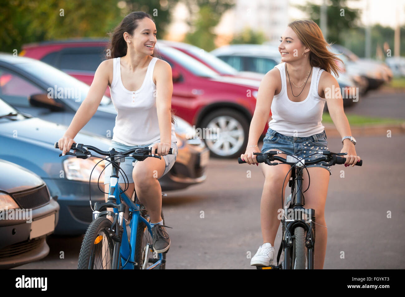 Due lieti di ridere bella bionda e bruna di donne giovani amici guardando ogni altro, equitazione in giocoso concorso bici accanto a Foto Stock